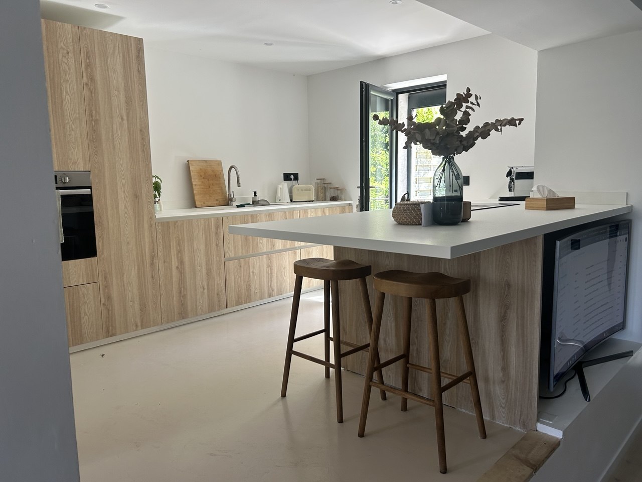 Cuisine ouverte rénovée par Rénova Habitat : façades bois clair, îlot central et sol en béton ciré